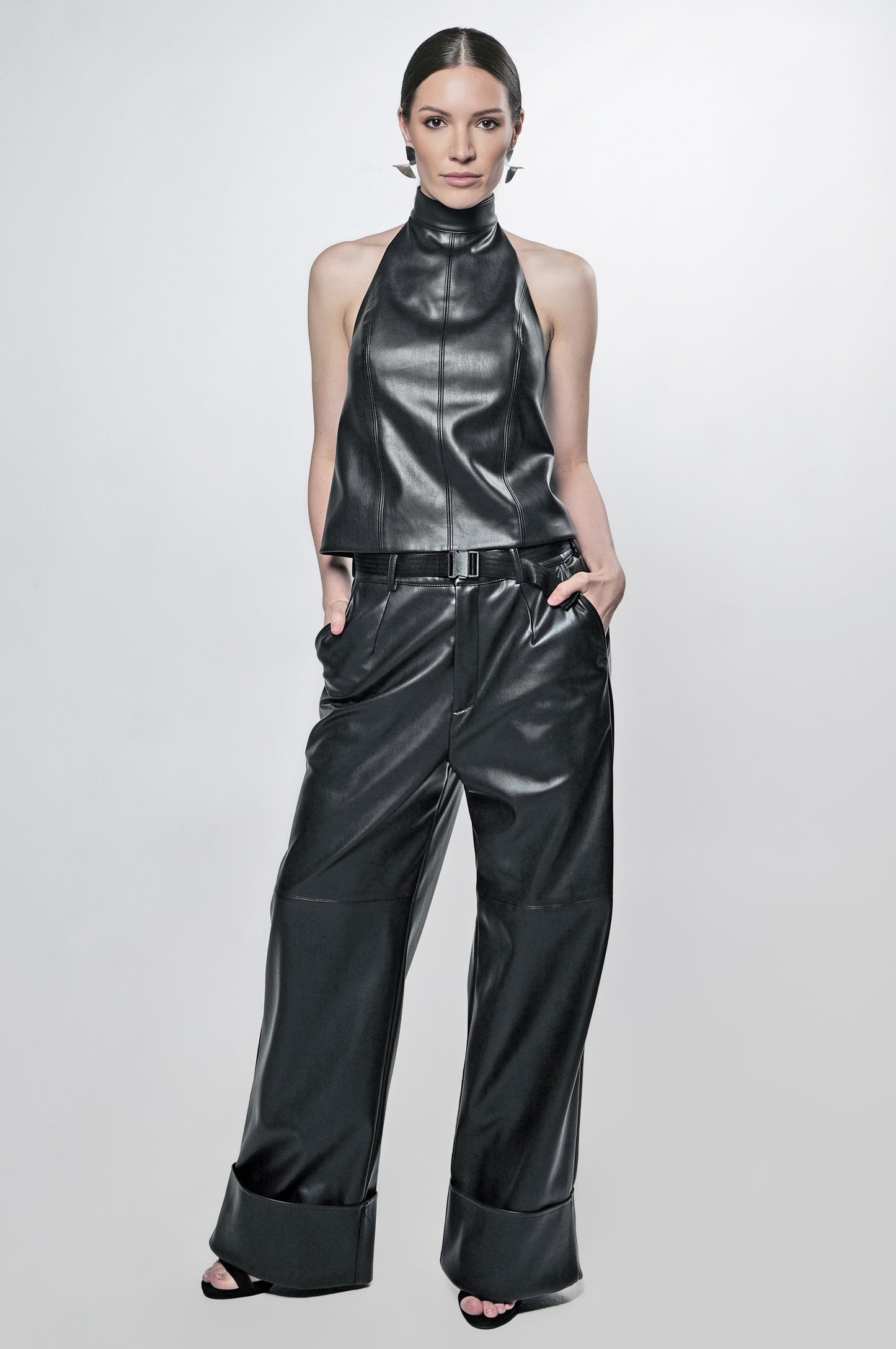 Model wearing modern black vegan leather halter top and black leather cuff wide leg pants