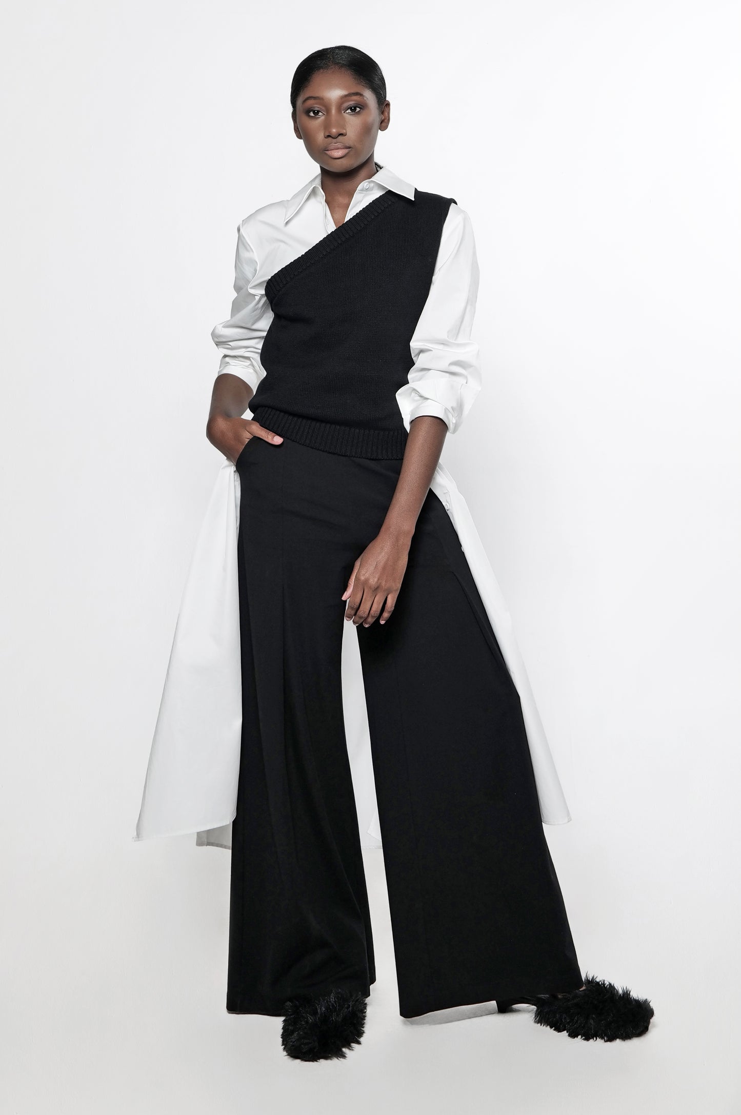 A model wearing a one shoulder asymmetric knit vest in black with black wide leg pants