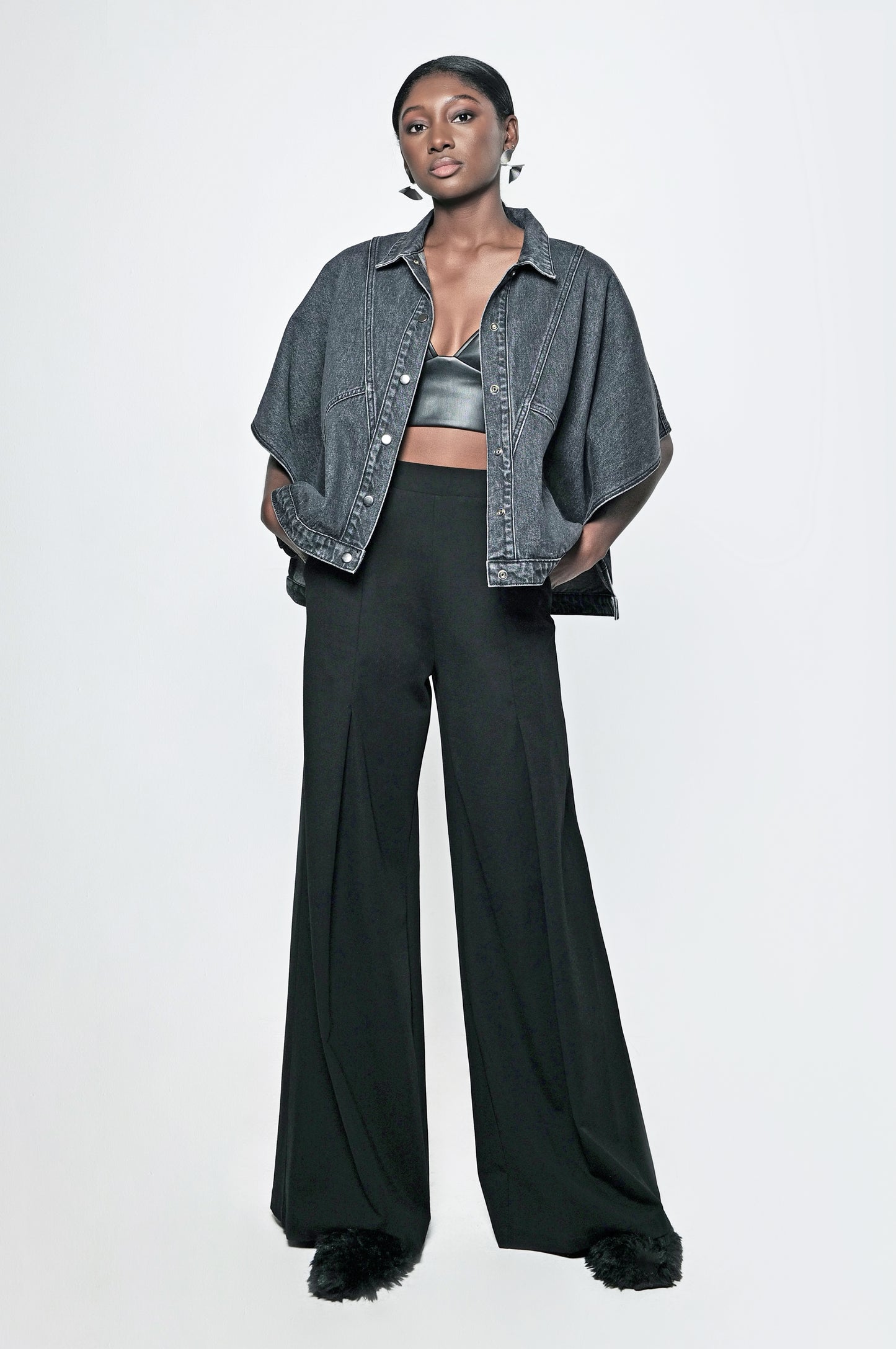 A woman wearing a black denim cape jacket and black pants. The jacket has front pockets and a relaxed fit.