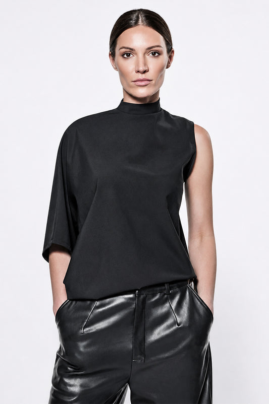 Model wearing a black mock neck one sleeve top against a white background.