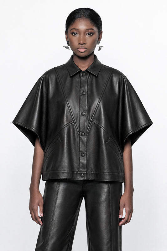A model wearing a black leather-like short-sleeve button-front top with a collar and matching black leather pants, photographed against a plain light gray studio background.