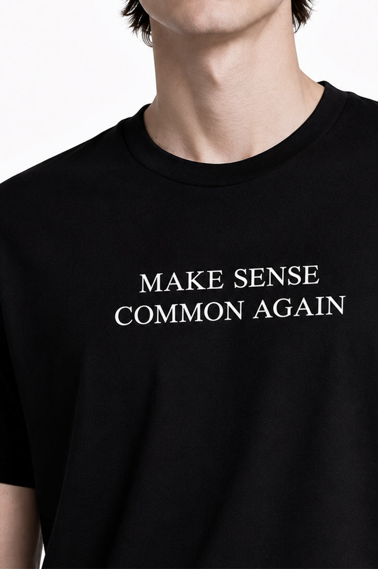 Close up of man wearing a black t-shirt that says "Make Sense Common Again" in white text